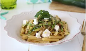 Pasta fredda con zucchine grigliate e cubetti di formaggio fresco, guarnita con erbe aromatiche. Un piatto estivo leggero e gustoso.