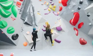 Zwei Frauen bouldern an einer Kletterwand. Eine gibt Anweisungen, die andere klettert. Das ist, was ist bouldern: eine Herausforderung für Körper und Geist.