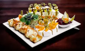 Talerz z przekąskami finger food: ciastka francuskie, sery, pomidorki koktajlowe, oliwki i dżem.