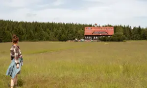 Dziewczyna w kratę podziwia krajobraz w Górach Izerskich. W oddali schronisko i las.