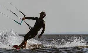 Kitesurfer w kasku i piance, z latawcem i deską, tworzy rozpryski wody na jeziorze.