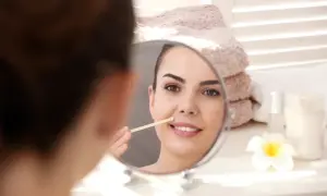 Kobieta w lustrze usuwa wąsik patyczkiem. Szuka sposobu, jak usunąć wąsik żeby nie odrastał.