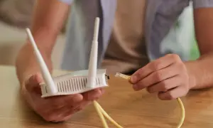 Mężczyzna podłącza kabel Ethernet do routera, pokazując, jak podłączyć wzmacniacz wifi.