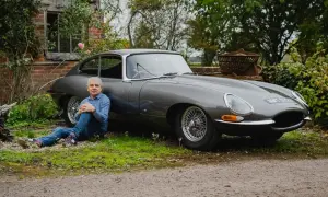 Man sitter vid en grå Jaguar E-Type i lantlig miljö.