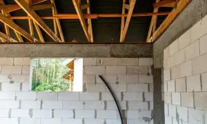 Widok wnętrza budowy z bloczków betonowych, widoczna konstrukcja dachu. To etap prac, który przybliża do momentu, jak zrobić wieniec budowlany.