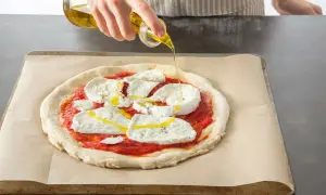 Oliwa z oliwek spływa na pizzę z mozzarellą i sosem pomidorowym, przygotowywaną w Thermomixie.