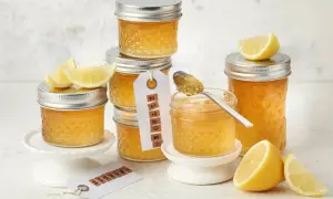 Gläser mit leuchtend gelber Zitronenmarmelade, garniert mit frischen Zitronenspalten. Ein Löffel mit Marmelade zeigt die köstliche Konsistenz, perfekt für ein Zitronenmarmelade Rezept.