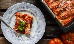 En portion läcker cannelloni med tomatsås och basilika på en vacker tallrik. Bredvid syns en ugnsform med mer cannelloni och färska tomater. Ett perfekt cannelloni recept!