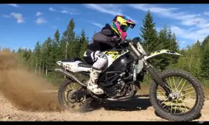 Motocyklista w kolorowym kasku pędzi na crossie, wzbijając tumany kurzu.