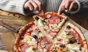 Une personne choisit une part de pizza avec une riche pizza garniture : jambon, œufs, olives, artichauts et champignons.