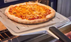 Une délicieuse pizza maison dorée et gratinée sort du four sur une pelle à pizza.