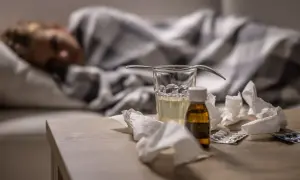 Sjuk person i sängen med medicin, glas vatten och näsdukar på bordet. Viktigt för att minska sjukfrånvaro.
