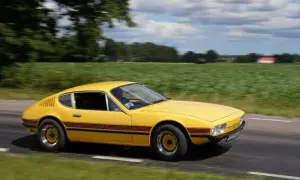 Gul vw sp2 susar fram längs en landsväg, med gröna fält och moln som suddas ut i bakgrunden.