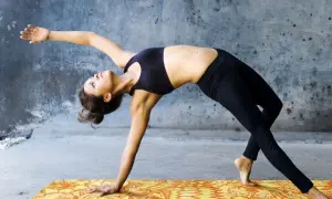 Donna in posizioni di yin yoga, con un braccio teso e il corpo arcuato all'indietro, su un tappetino colorato.