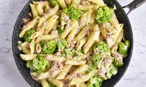 Makaron penne z tuńczykiem i brokułami w kremowym sosie w czarnej patelni.