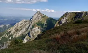 Widok na skaliste szczyty i zielone zbocza. Na pierwszym planie trawy, w oddali dolina małej łąki.