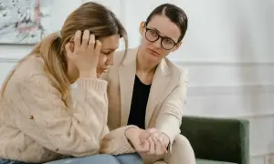 Kobieta w beżowym żakiecie pociesza smutną koleżankę. Czasem nawet urlop siła wyższa nie pomaga, gdy potrzebujemy wsparcia.