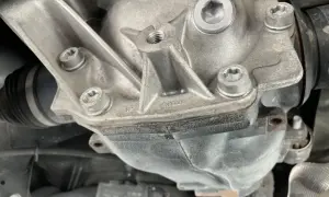 Metalowy dyferencjał z widocznymi śrubami i osłoną przegubu napędowego.