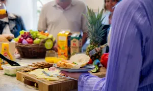 En härlig frukost på jobbet med frukt, ost, kex och färska bullar. En person tar en smörgås.