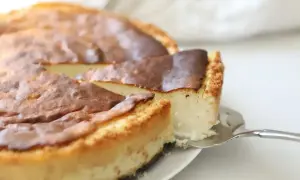 Kawałek bardzo puszystego sernika z wiaderka, z lekko przypieczoną skórką, jest podnoszony łopatką.