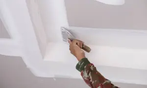 Mano aplicando masilla para techo escayola con espátula, alisando juntas y esquinas para un acabado perfecto.