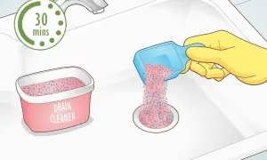 Rękawica w żółtej rękawiczce wsypuje granulat do odpływu zlewu. Obok stoi pojemnik z napisem "DRAIN CLEANER". Czas oczekiwania to 30 minut.