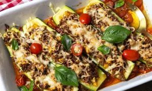 Herzhafte zucchini schiffchen mit Hackfleisch und Käse überbacken, garniert mit frischem Basilikum und Kirschtomaten.