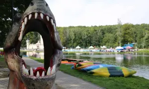 Smok otwiera paszczę, zapraszając do odkrywania magicznych miejsc opolskich. W tle jezioro, basen i kolorowe kajaki.