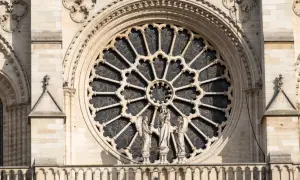Ein Rosettenfenster im Stil der Gotik-Kunst, umrahmt von Steinfiguren und filigranen Verzierungen an einer Kathedrale.