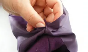 Dłoń trzyma fioletowy materiał bluzy, pokazując jak skrócić rękawy.