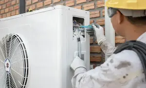 Technik w żółtym kasku reguluje okablowanie pompy ciepła, co może pomóc w optymalizacji jej pracy, np. jak zmniejszyć taktowanie pompy ciepła.