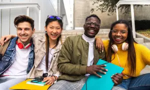 Cuatro jóvenes sonríen sentados en escaleras, planeando su futuro, quizás para trabajar en el extranjero.