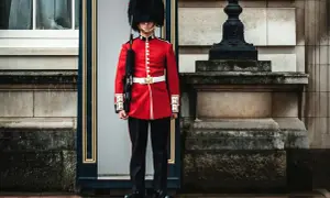 Un guardia con uniforme rojo y sombrero de piel, un típico inglés, vigila la entrada de un edificio histórico.