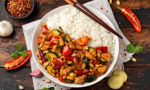 Pyszny kurczak kung pao z ryżem, papryką, cukinią i orzeszkami ziemnymi. Obok pałeczki, chili i czosnek.