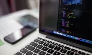 Laptop z kodem na ekranie, obok smartfon. Jak przyspieszyć laptopa? Optymalizacja kodu to klucz.