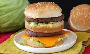 Domowy Big Mac z dwoma kotletami, serem, sałatą i sosem na talerzu.
