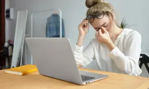 Zmęczona kobieta z okularami masuje oczy po pracy przy komputerze powyżej 4 godzin.