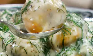 En sked lyfter upp en bit krämig dillstuvad potatis, täckt av färsk dill och en len sås.