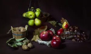 Scatti still life: mele rosse, pere verdi e rosse, noci in un cesto di legno e castagne su un tronco.