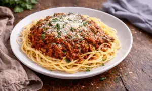 Talerz spaghetti z sosem bolońskim, posypany parmezanem i natką pietruszki.