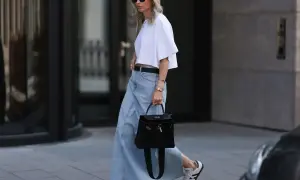 Stylowa kobieta w jasnej, jeansowej spódnicy midi i białym crop topie, z czarną torebką i sneakersami.