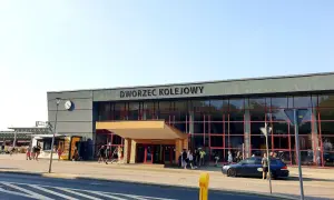 Dworzec kolejowy w Krakowie, z ludźmi i samochodami przed wejściem.