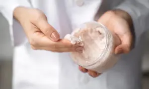 Dłonie w białym kitlu pobierają z pojemnika drobnoziarnisty peeling. To świetny sposób, by dowiedzieć się, co to mocznik i jak działa na skórę.