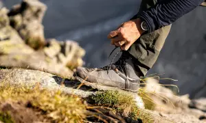 Mężczyzna sznuruje buty trekkingowe na kamieniu. Czy buty trekkingowe powinny być większe? Odpowiedź tkwi w komforcie i ochronie palców.