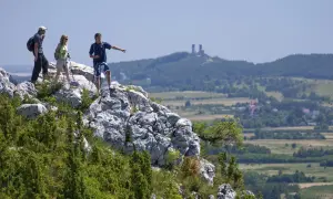 Trzech turystów na skale podziwia krajobraz Gór Świętokrzyskich. Jeden z nich wskazuje kierunek, gdzie widać ruiny zamku.