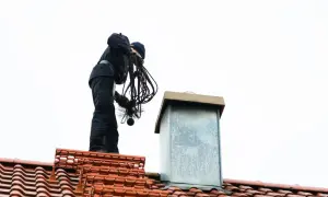 Kominiarz na dachu przygotowuje się do przeglądu komina, trzymając szczotkę i liny.