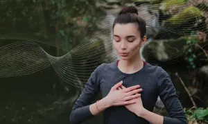 Kobieta z zamkniętymi oczami praktykuje techniki oddychania pranayama na tle natury.