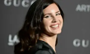 Uśmiechnięta Lana Del Rey, artystka znana z nastrojowych piosenek, na tle logo Gucci.