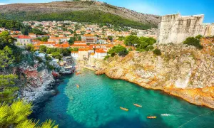 Kajaker på tur i det turkosa vattnet vid Gamla stan Dubrovnik, med klippor och stadens takåsar i bakgrunden.