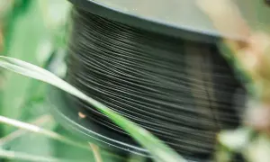 Nawinięta na szpulę ciemna żyłka na spinning, otoczona zieloną trawą. Idealna do połowu drapieżników.